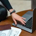 Close-up of a person typing on a laptop with legal documents on a table, showcasing work and technology integration.