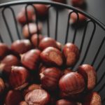 A close-up view of fresh organic chestnuts in a black wire basket, highlighting their rich texture.