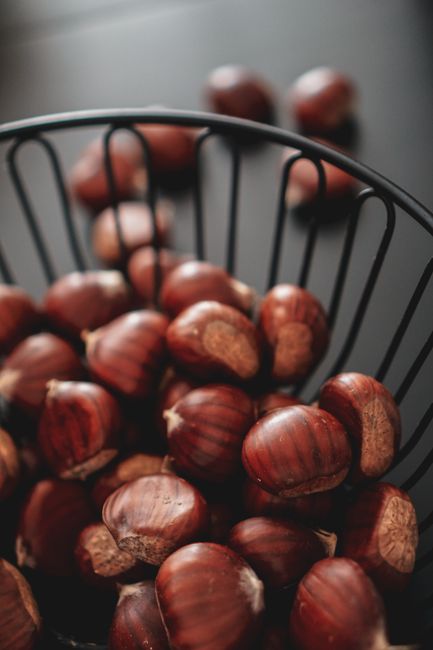 A close-up view of fresh organic chestnuts in a black wire basket, highlighting their rich texture.